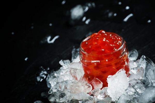 خاویار قرمز خوشمزه در یک شیشه شیشه ای روی یخ خرد شده در زمینه سنگ سیاه فوکوس انتخابی