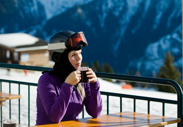زن جوانی که بعد از اسلالوم در فضای باز با یک فنجان چای در کافه کوه استراحت می کند