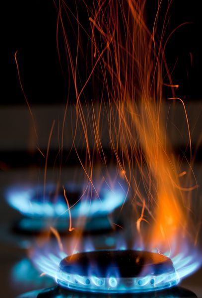 جرقه ها و شعله های آتش بالای اجاق گاز که با شعله های آبی می سوزد