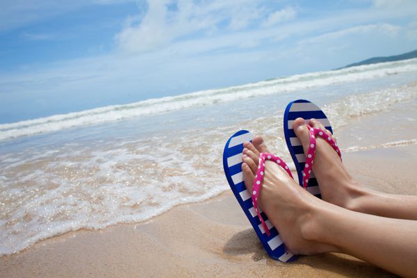 پاهای دختر جوان با صندل های دمپایی رنگارنگ در ساحل دریا