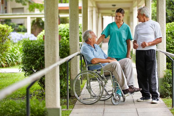 دو شهروند سالخورده در حال صحبت با یک پرستار در باغ بیمارستان