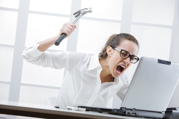 زن تاجری وحشت زده با چکش آماده شکستن کامپیوتر لپ تاپ خود است