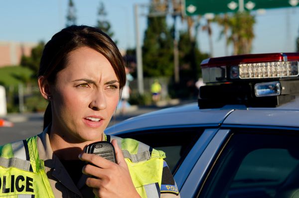 یک افسر پلیس زن که کنار ماشینش ایستاده و می خواهد در رادیو صحبت کند