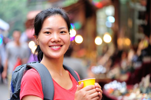 زن آسیایی سفر با یک فنجان قهوه در خیابان لبخند می زند