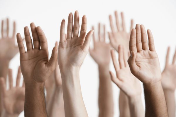 نمای نزدیک از مردان و زنان چند قومیتی که دست ها را در برابر پس زمینه سفید بالا می برند