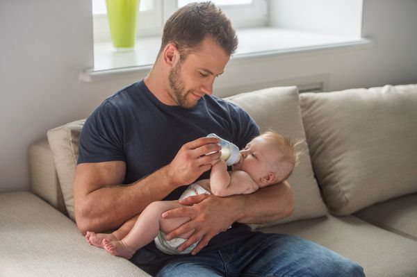 مرد با بچه مرد جوان عضلانی که به نوزاد کوچک شیر می دهد