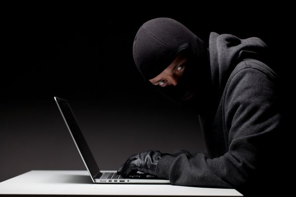 هکر کامپیوتری در یک کلاهک که در تاریکی کار می کند و داده ها و اطلاعات هویتی شخصی را از رایانه لپ تاپ می دزدد