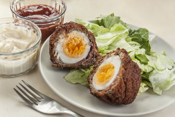 تخم مرغ اسکاچ - تخم مرغ آب پز ارگانیک آزاد در لایه ای از گوشت سوسیس پیچیده شده در بیکن رگه دار پوشیده شده در نان ترد و سرخ شده در روغن نباتی