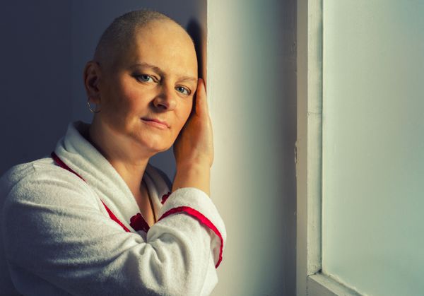 زن طاس مبتلا به سرطان که جلوی پنجره بیمارستان ایستاده است
