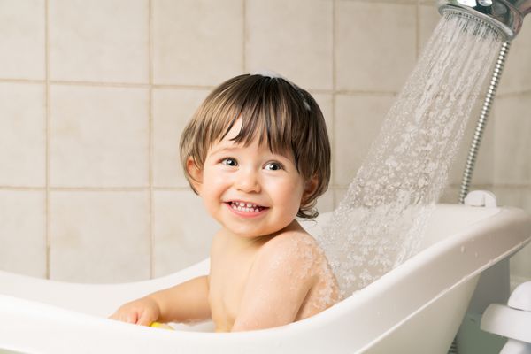 خندان پسر بچه زیبا در حال حمام کردن در وان با دوش در خانه