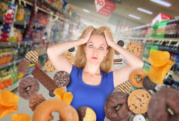 زنی در یک خواربارفروشی دور خود تنقلات شیرینی دارد او ترس دارد و دونات و کلوچه وجود دارد از آن برای یک مفهوم سلامتی یا رژیم غذایی استفاده کنید