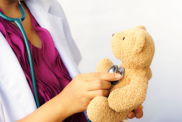 متخصص اطفال زن در حال معاینه یک خرس عروسکی با گوشی پزشکی