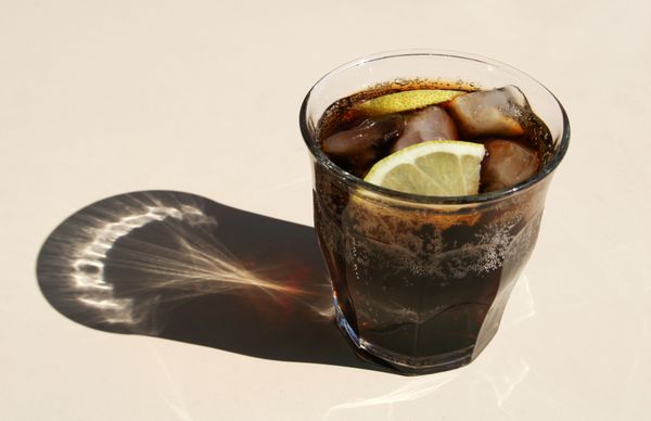 یک نوشیدنی کولا سرد با یخ و تکه‌های لیمو در یک لیوان در روز