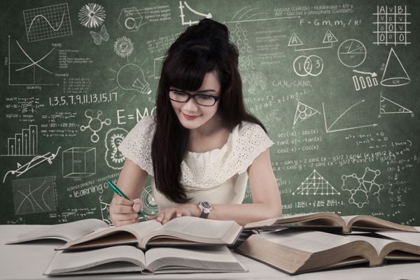 دانش آموز دختر در حال مطالعه در کلاس درس در حالی که منبع را روی کتاب می نویسد