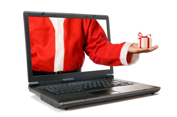 دست بابا نوئل با یک هدیه از صفحه یک رایانه لپ تاپ جدا شده در پس زمینه سفید بیرون می آید