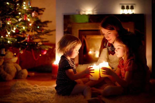 مادر جوان و دو دختر کوچکش در یک اتاق نشیمن تاریک دنج در شب کریسمس در کنار آتشفشان نشسته اند و شمع در دست دارند
