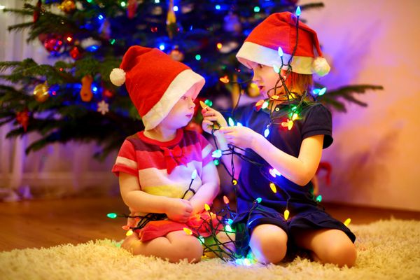 دو خواهر کوچک شایان ستایش در حال تزئین درخت کریسمس در خانه