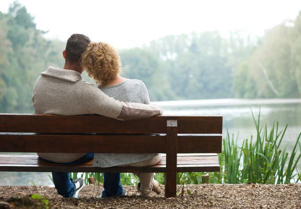 نمای عقب یک زوج شاد که کنار هم روی نیمکت در فضای باز نشسته اند