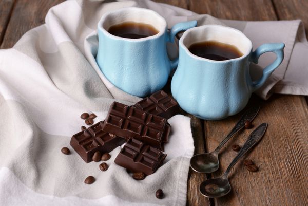 فنجان قهوه با شکلات و دستمال سفره روی میز چوبی