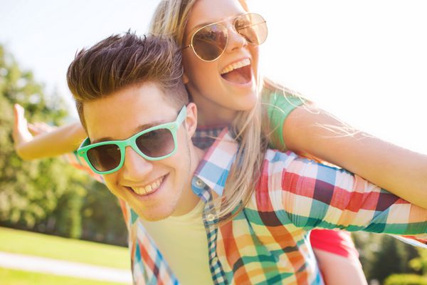 تعطیلات تعطیلات مفهوم عشق و دوستی - زوج نوجوان خندان با عینک آفتابی در حال تفریح در پارک تابستانی