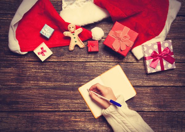 لیست آرزوهای نوشتن زن در دفترچه یادداشت نزدیک هدایای کریسمس