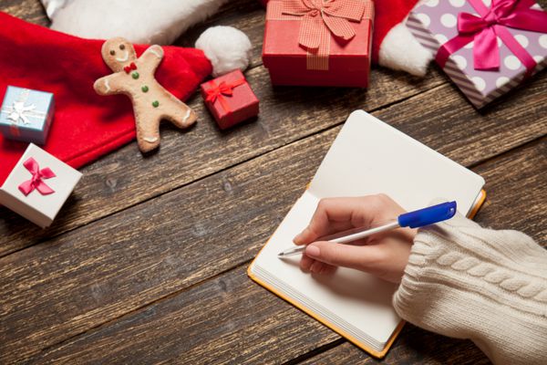 لیست آرزوهای نوشتن زن در دفترچه یادداشت نزدیک هدایای کریسمس