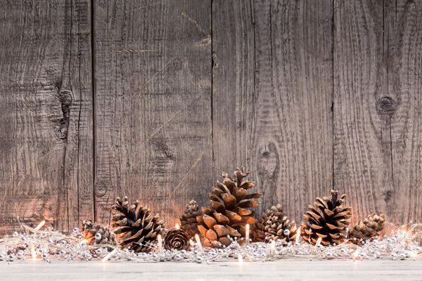 تزیین کریسمس با چراغ و مخروط صنوبر با زمینه چوبی طبیعی