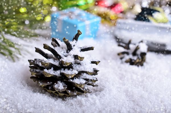 مخروط صنوبر در برف در پس زمینه تزئینات و هدایای کریسمس