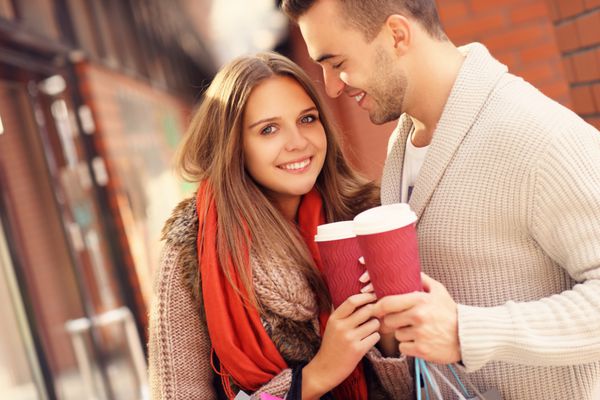 تصویری از یک زوج شاد در حال خرید در مرکز خرید با قهوه