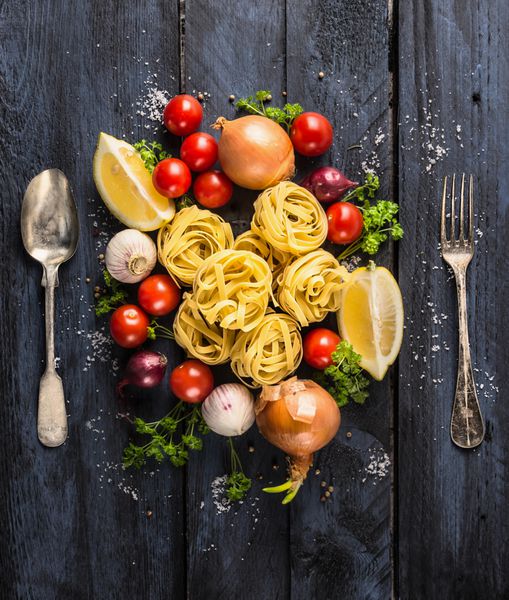 تالیاتله پاستا با گوجه فرنگی سبزیجات و ادویه جات برای سس گوجه فرنگی قاشق و چنگال در زمینه چوبی آبی تیره نمای بالا
