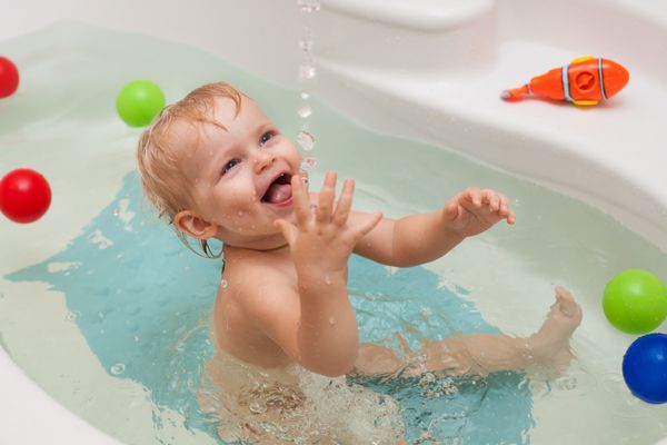 دختر بچه کوچولوی خنده دار در حمام با قطرات و پاشیدن آب
