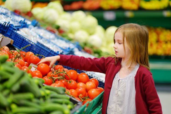 دختر بچه ای که در یک فروشگاه مواد غذایی گوجه فرنگی انتخاب می کند