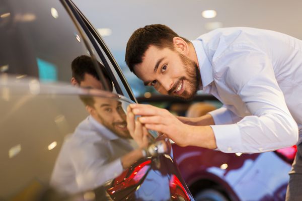 تجارت خودرو فروش خودرو مصرف گرایی و مفهوم مردم - مرد خوشحال در حال لمس ماشین در نمایشگاه یا سالن خودرو