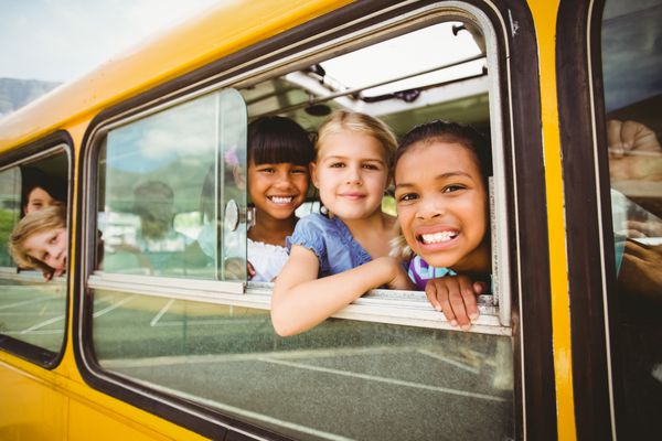دانش آموزان ناز در اتوبوس مدرسه در خارج از مدرسه ابتدایی به دوربین لبخند می زنند