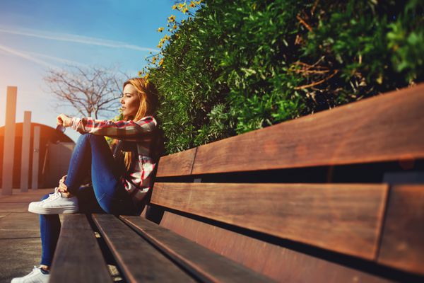 نمای جانبی زن نشسته روی نیمکت در حال لذت بردن از طبیعت در روز آفتابی در فضای باز دختر جوان جذاب در حال استراحت در پارک بهار دانشجوی دختر در حال استراحت در محوطه دانشگاه نور خورشید شعله ور