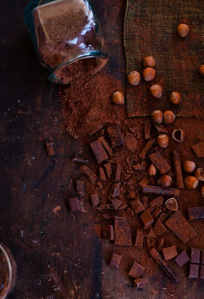 یک پشته از شکلات های مختلف مقدار زیادی شکلات رنده شده تکه هایی از شکلات تیره و شیری پودر کاکائو و مغز فندق که روی میز پرنعمت تیره گرفته شده است سبک روستیک نمای بالا