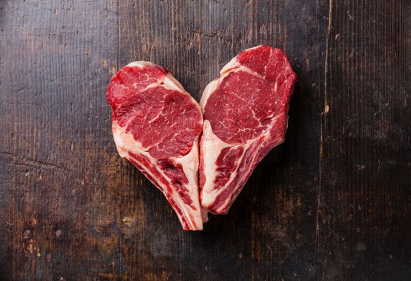 استیک گوشت خام ریبی شکل قلب روی زمینه چوبی