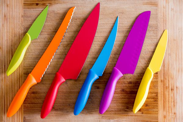 چاقوهای رنگارنگ آشپزخانه با اهداف مختلف در بالای یک تخته برش چوبی در نمای با زاویه بالا گرفته شده است