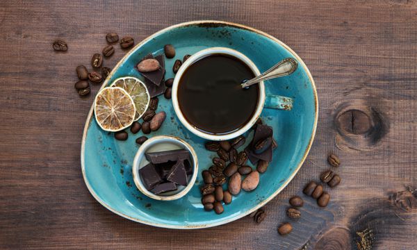 قهوه سیاه در فنجان آبی قدیمی و شکلات روی تخته های چوبی تیره قدیمی