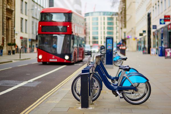 ردیف دوچرخه برای کرایه با اتوبوس دو طبقه قرمز در پس زمینه در خیابانی از لندن انگلستان