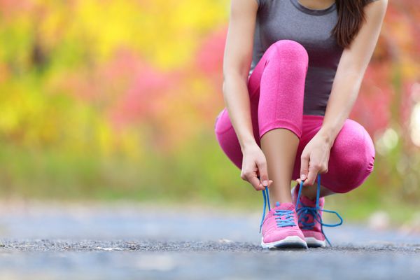 کفش دویدن - زن در حال بستن کفش ls نمای نزدیک از دونده تناسب اندام ورزشی زن که برای دویدن در فضای باز در مسیر جنگلی در اواخر تابستان یا پاییز آماده می شود