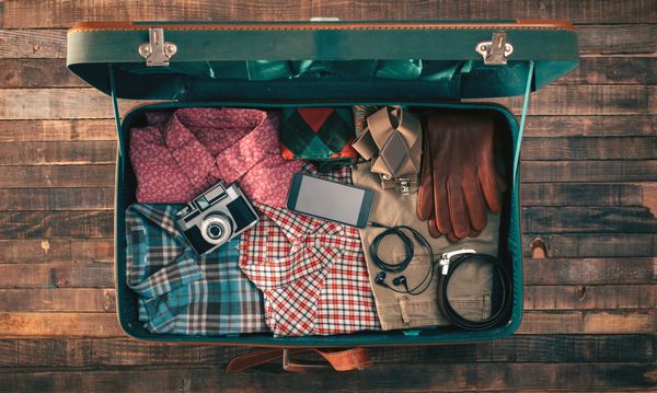 بسته بندی مسافرتی هیپستر قدیمی چمدان باز روی میز چوبی با لباس دوربین و تلفن همراه نمای بالا