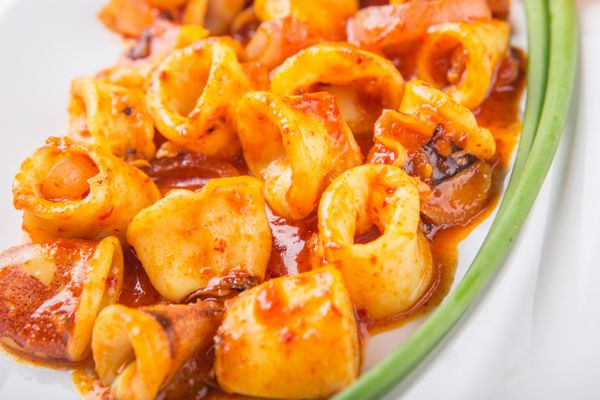 غذای مالزیایی از ماهی مرکب سرخ شده با سامبال تند و سس چیلی با پیازچه و گوجه فرنگی در بشقاب سفید
