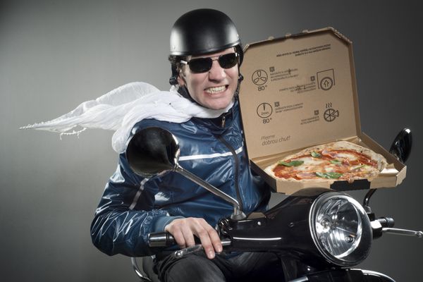 تحویل پیتزا مردی سوار بر موتور که پیتزا در دست دارد