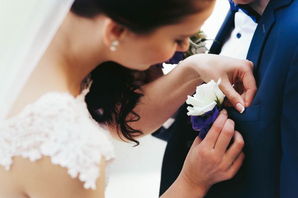 عروس مجعد جوان زیبا و شیک در حال سنجاق کردن گلها به دامادش است