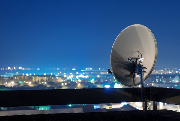 آنتن بشقاب ماهواره در بالای ساختمان در منطقه شهری در شب