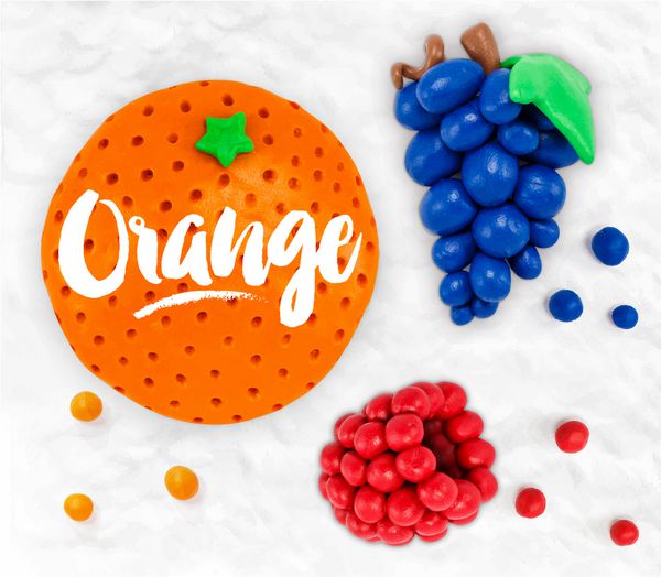 میوه‌های انگور نارنجی تمشک مدل‌سازی شده از پلاستین که روی پس‌زمینه‌ی پلاستیکی سفید روی هم قرار گرفته‌اند