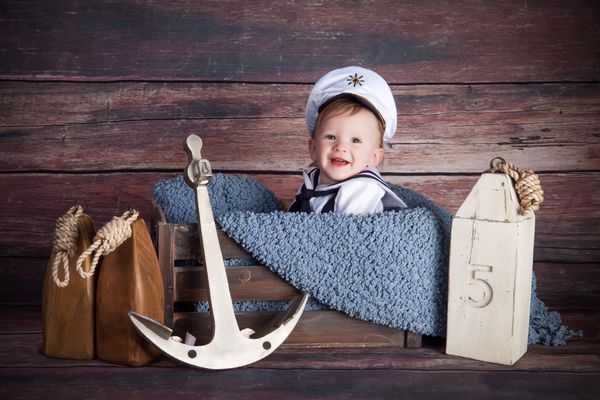 یک نوزاد پسر شایان ستایش که با وسایل دریایی ژست می گیرد لبخند می زند و لباس ملوانی پوشیده است