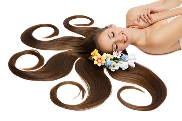 زن جوان زیبا با موهای طبیعی بسیار بلند و گل هایی روی آن به پشت خوابیده است با زمینه سفید مجزا شده است