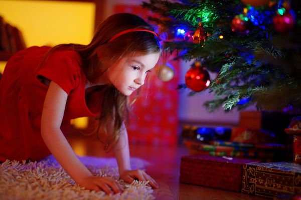 دختر کوچولوی شایان ستایشی که به دنبال هدیه زیر درخت کریسمس در شب کریسمس در خانه است
